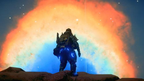 A man stands at the top of a rocky hilltop. His back to the viewer. He looks out towards the night sky that is filled with a variety of bright, stunning colours that cover his field of view. The sky's pattern is circular with the following colours from center to outside: blues, cyan, white, yellow, orange and red.
