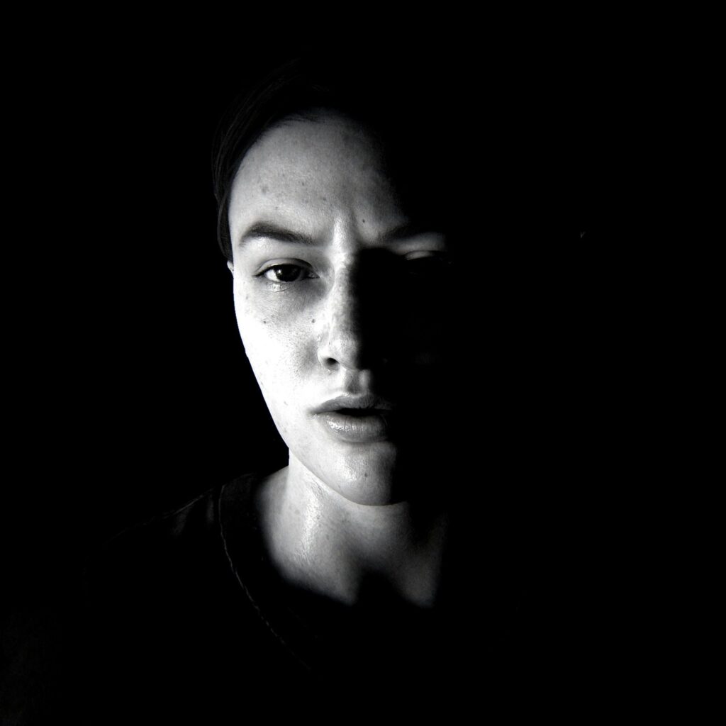 Black and white image of a woman's face, in a shadow and surrounded by blackness
