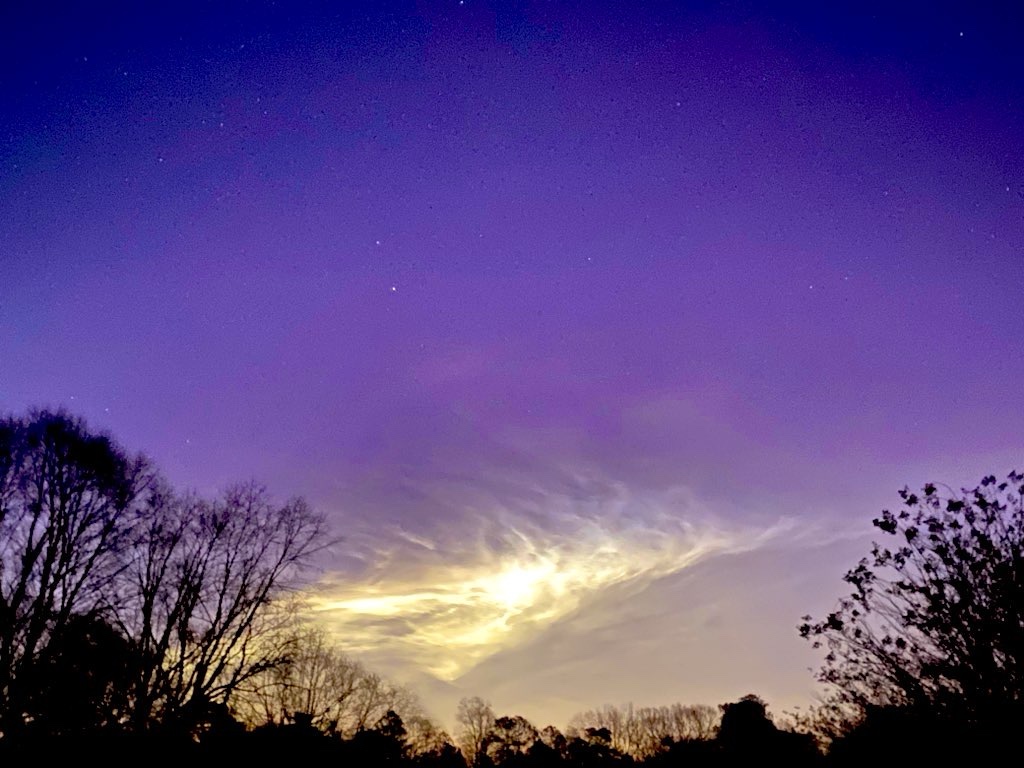 A purple sky fading into sunrise or sunset. Trees silhouette in bottom of image