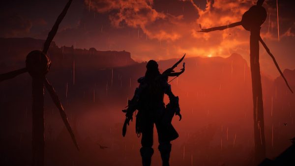 A red hazy fog covers the distant hills where the sun is creeping over the brow. A woman's silhouette stands in the foreground looking out towards that sun. She stands between two rusted, broken wind turbines. A bow is carried on her back.